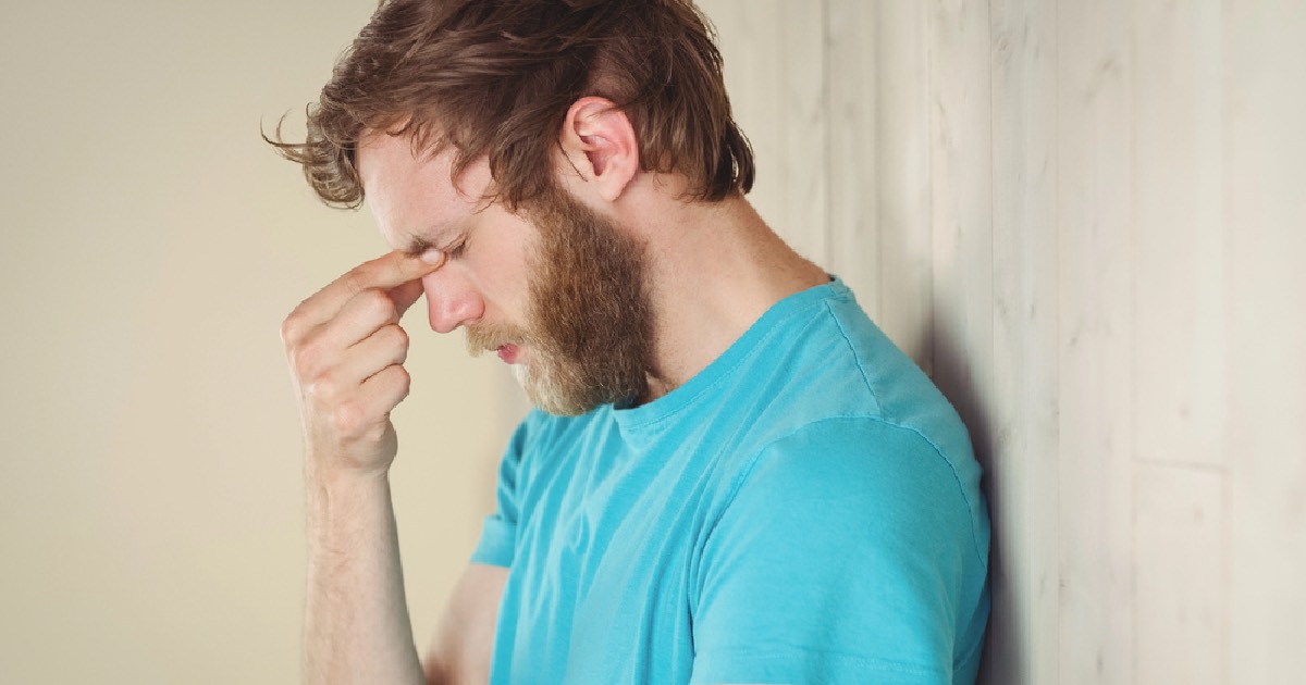 Young man leaning against wall rubbing his temples