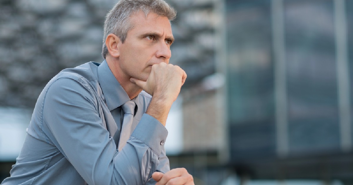 Man in suit with hand over his face thinking 