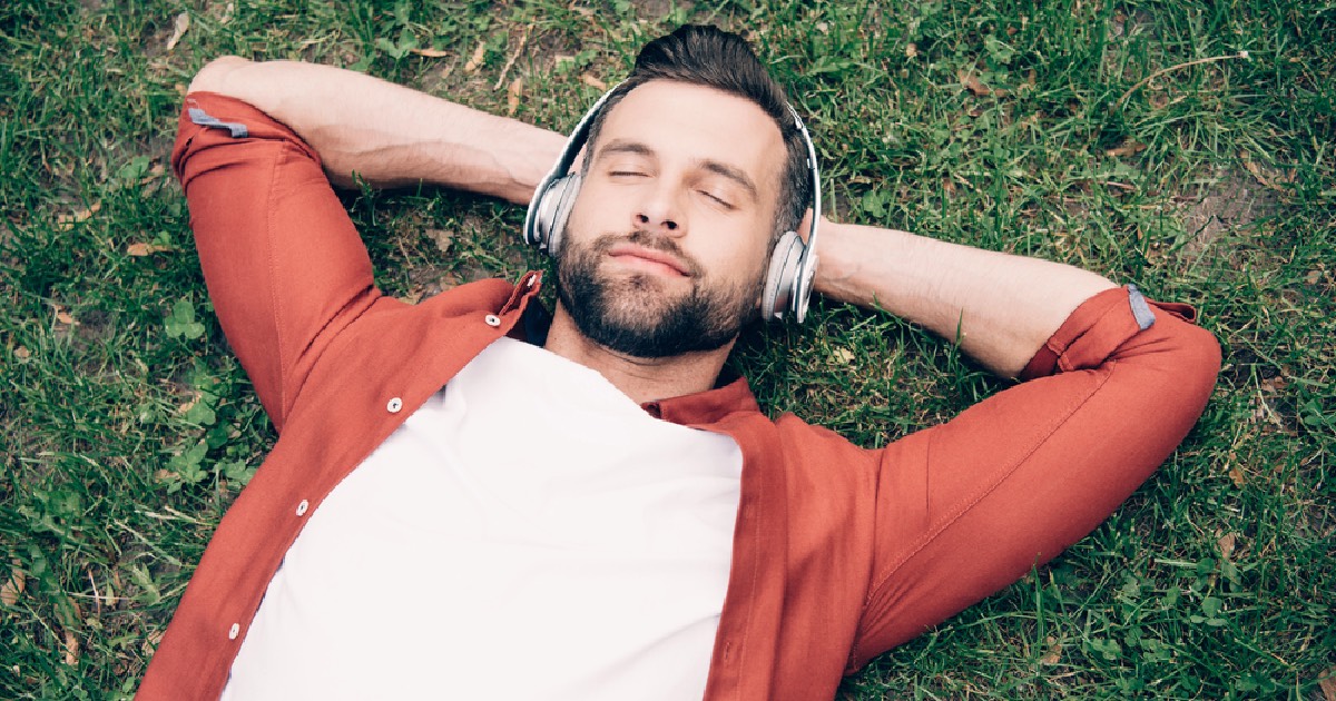 young man laying on grass while listening to music 