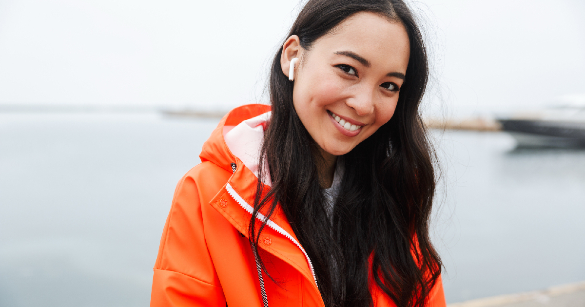 Attractive Asian woman wearing orange coat, walking along water