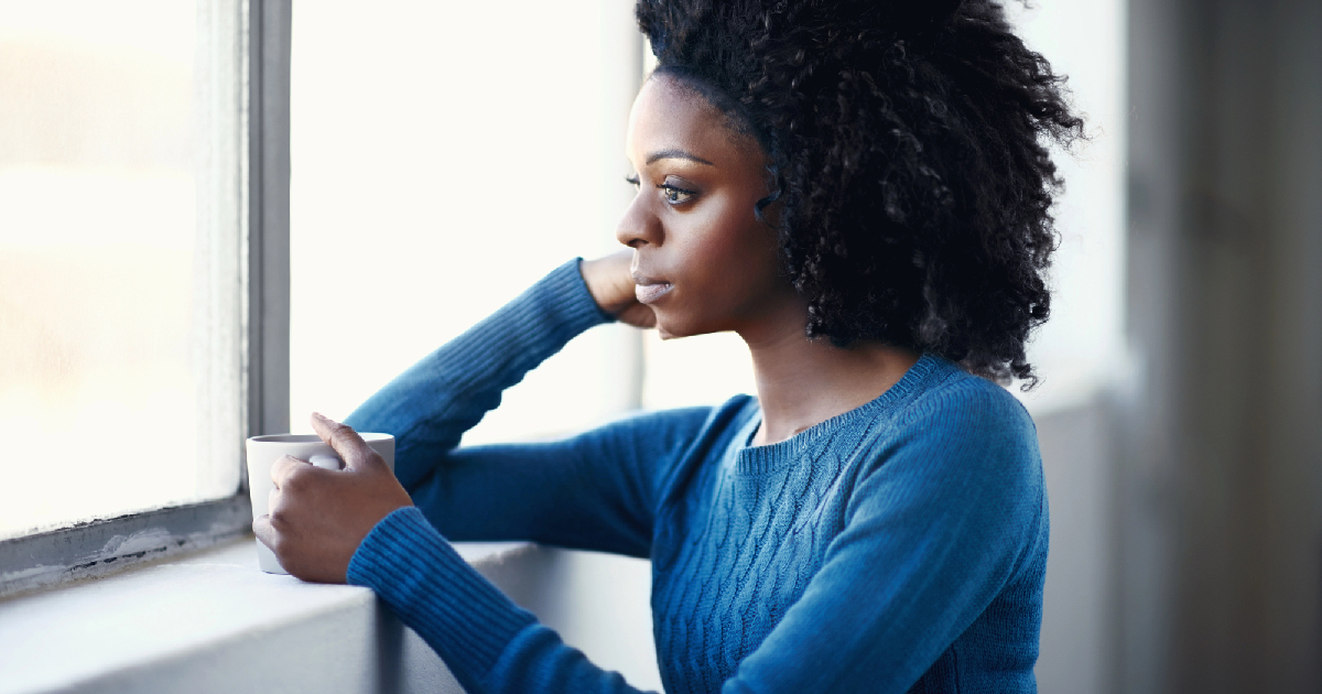 Young woman looking out window holding cup of coffee