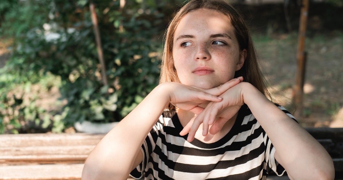Young freckled girl sitting outdoors
