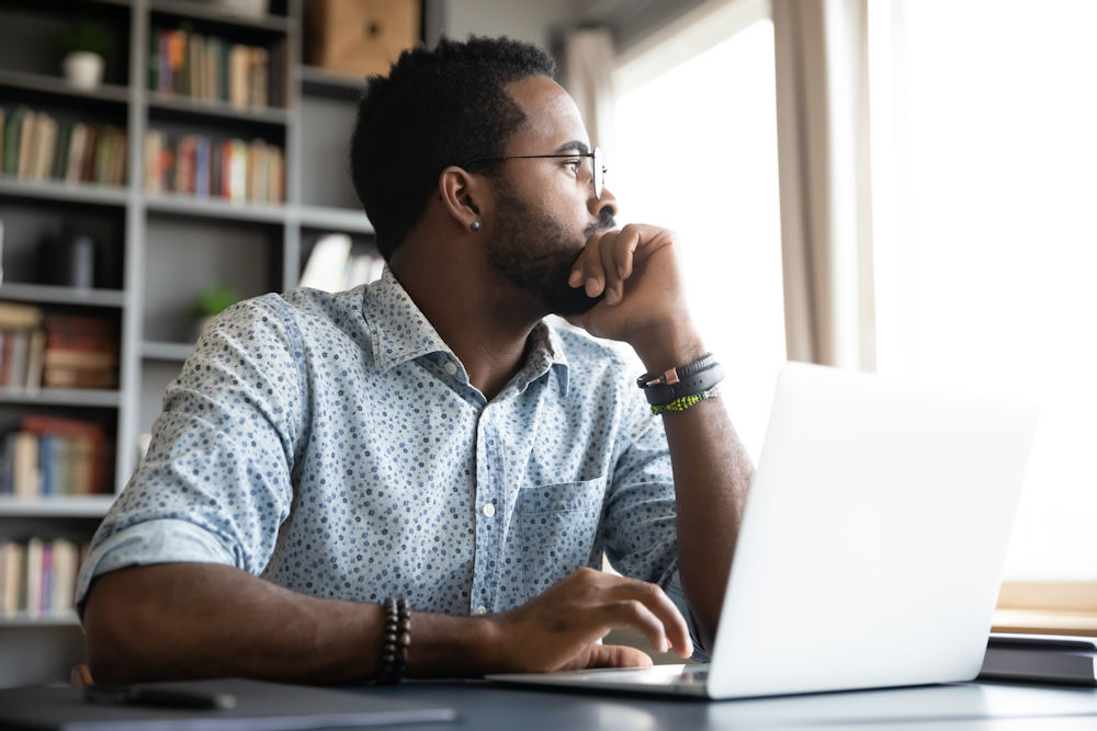 Thoughtful serious african man sit with laptop thinking of project